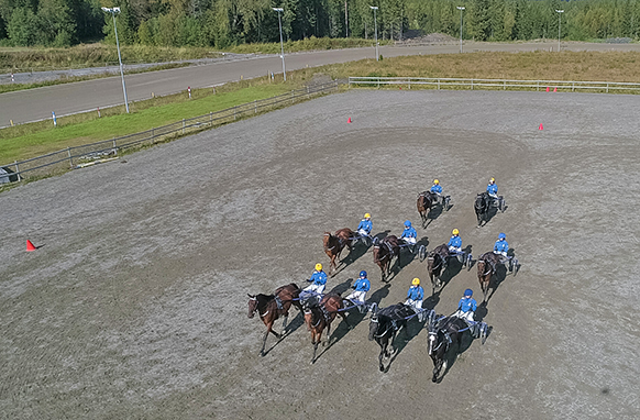Tio travekipage kör i formation på en utomhus körplan.