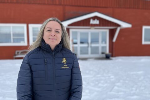 Kvinna står framför en röd byggnad med texten Aula på.