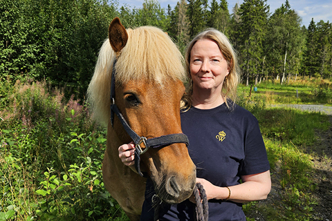 Man kvinna står och håller en islandshäst. Hon har mörkblå t-shirt med Wångens emblem på.