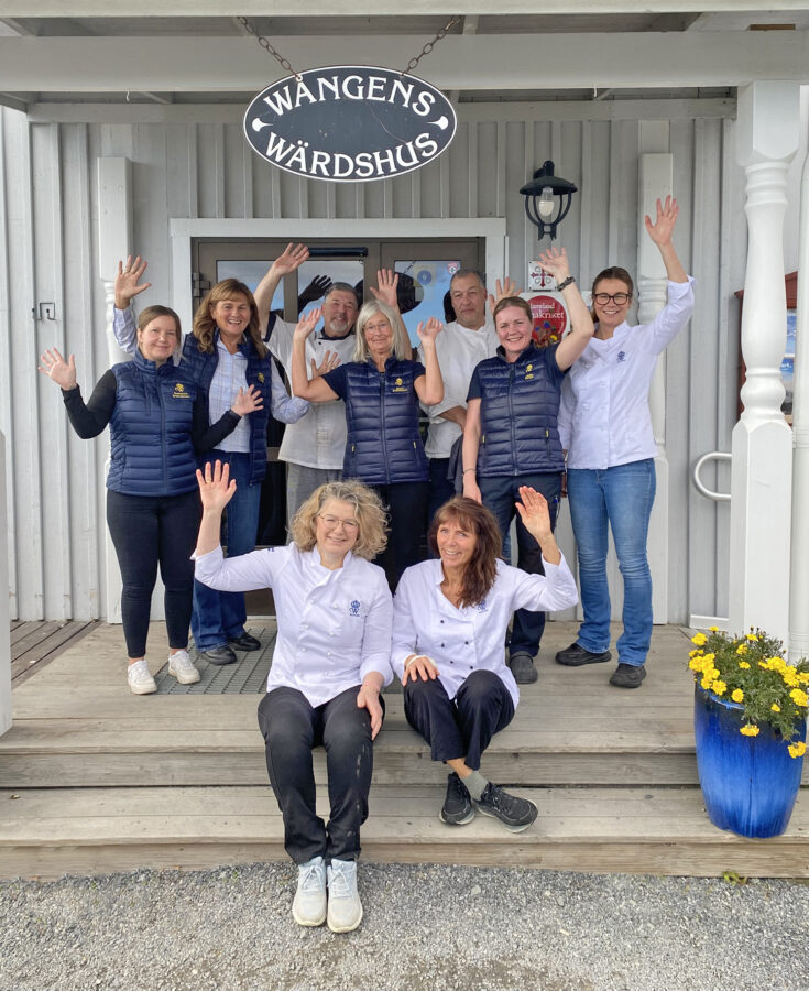 Grupp glada medarbetare vinkar från trappen till Wångens wärdshus