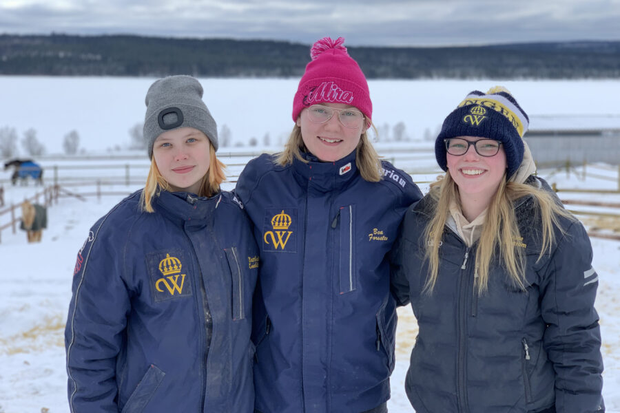 Tre Wångenelever står i en hästhage. Det är vinter och de har mössor och Wångenjackor på sig.