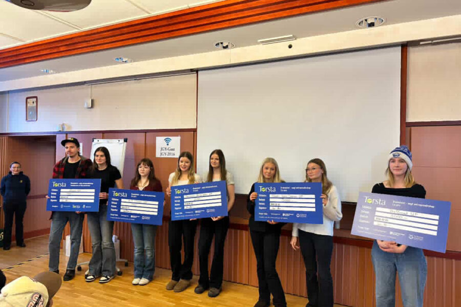 Elever på rad i ett klassrum håller i stora prischeckar