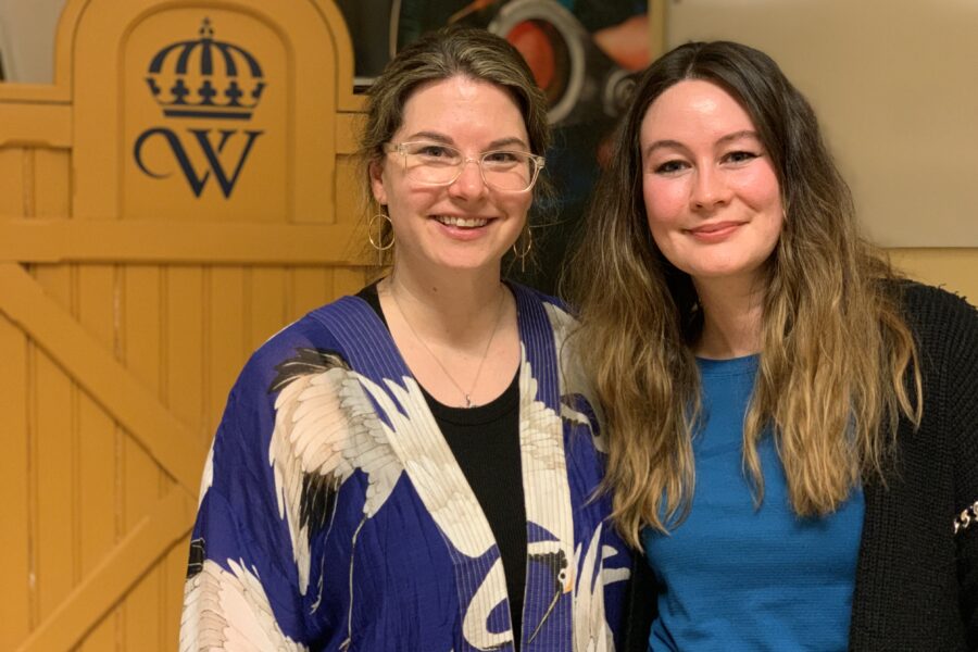 Två kvinnor står sida vid sida och ler mot kameran, bakom syns en gultalarstol med Wångenemblemet på