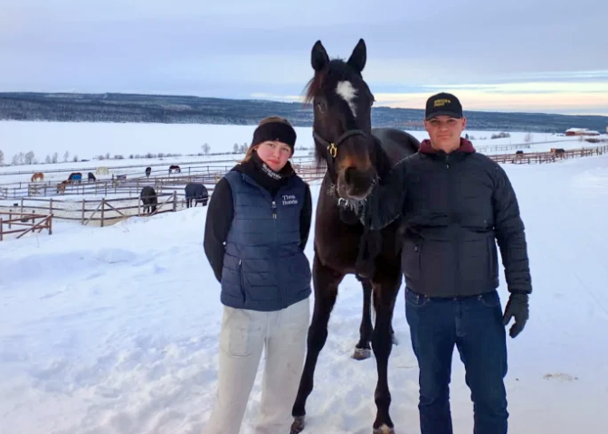 Gymnasieeleverna Thea och Conrad står på varsin sida om en varmblodstravare utomhus på Wången en vinterdag.