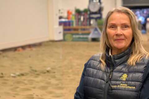 Kvinna står i en ridarena med blå väst med namnet Annie von Krusenstierna på