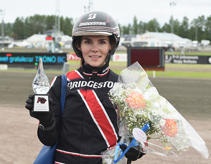 Jill Ivarsson i hjällm och svartröd kuskdräkt håller i en pokal och blombukett.