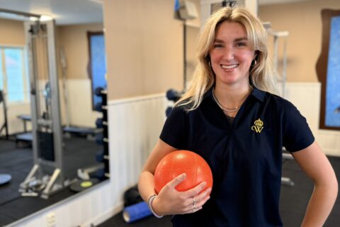 Leende kvinna håller en orange träningsboll i ett gym