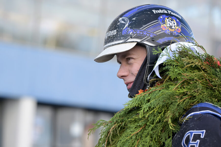 En kusk i hjälm syns i profil med en lagerkrans runt halsen.