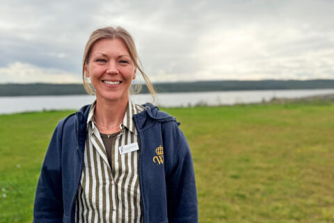 Leende kvinna står på en gräsmatta vid en sjö under molnig himmel