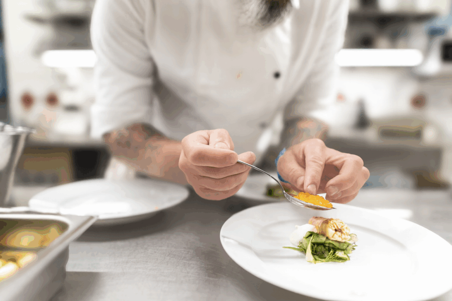 I ett livligt restaurangkök serverar en kock i en orörd vit uniform skickligt mat med en sked.