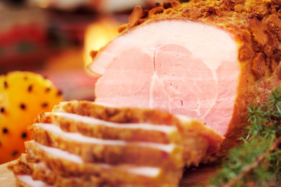 Skivad julskinka ligger upplagt mellan en nejlikedekorerad apelsin och grönkål