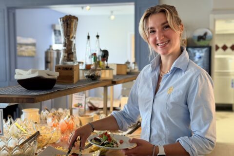 Blond kvinna i ljusblå skjorta med Wångens emblem, står vid salladsbuffén i en restaurang.